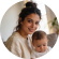 Smiling woman holding a baby in a cozy indoor setting.