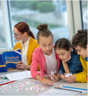 Person sitting on a stool reading a newspaper against a plain background.