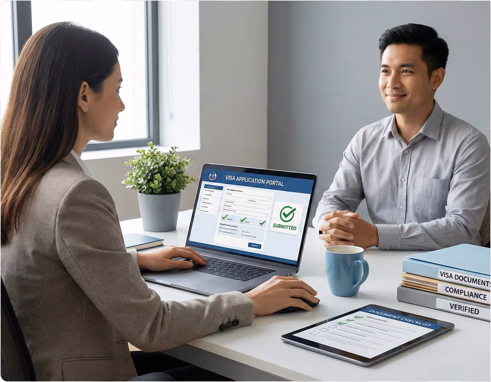 Two professionals at a desk, with a woman submitting a visa application on a laptop and a man sitting across, smiling.