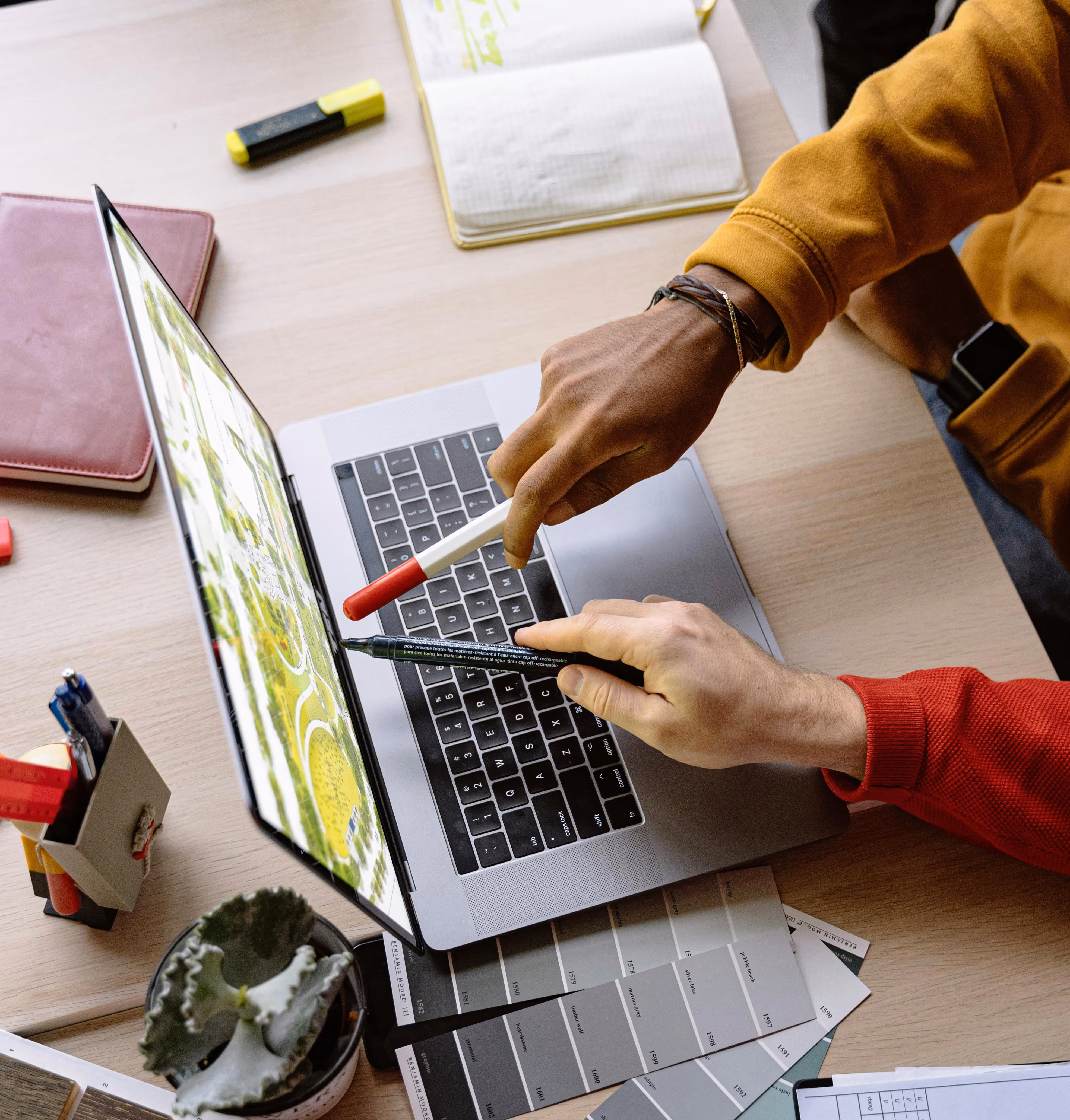 Business partners reviewing work on a laptop at a desk with documents, samples, and office tools, symbolizing active business operations and collaboration.