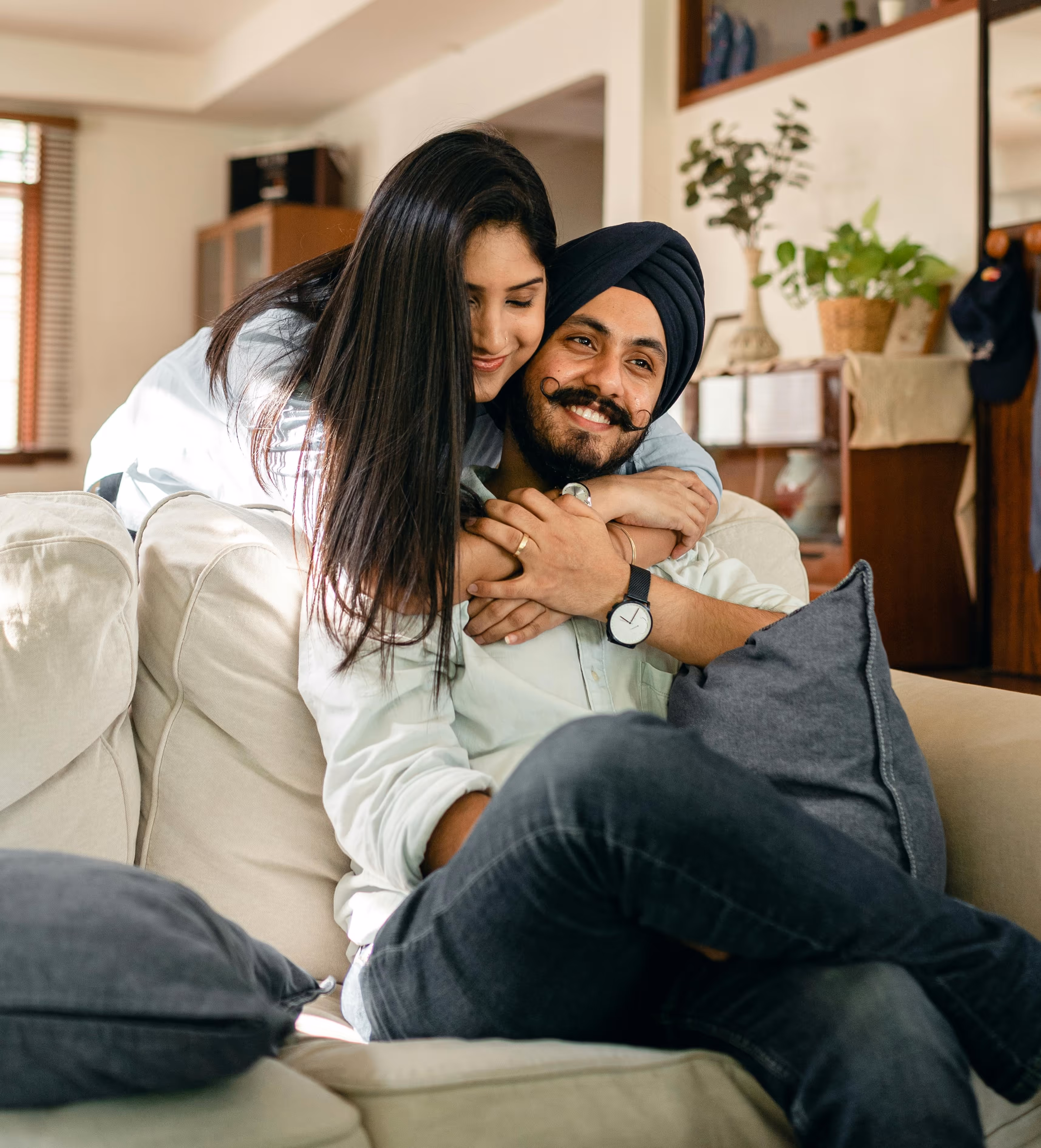 A happy couple embracing on a sofa at home, representing family life, stability, and settling in Australia.