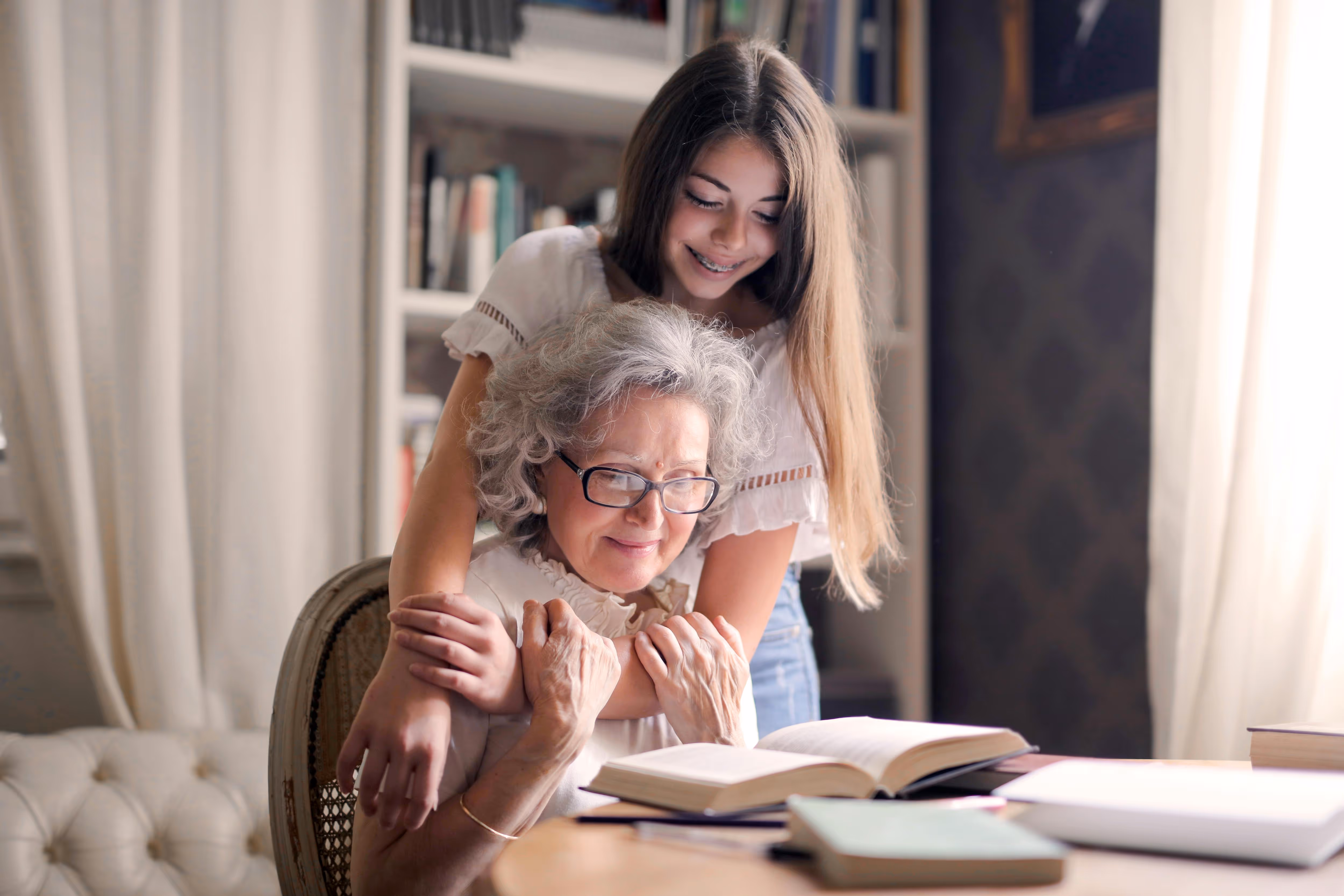 Young girl hugging her grandmother while reading together at home, representing family bonds, care, and reunification in Australia.