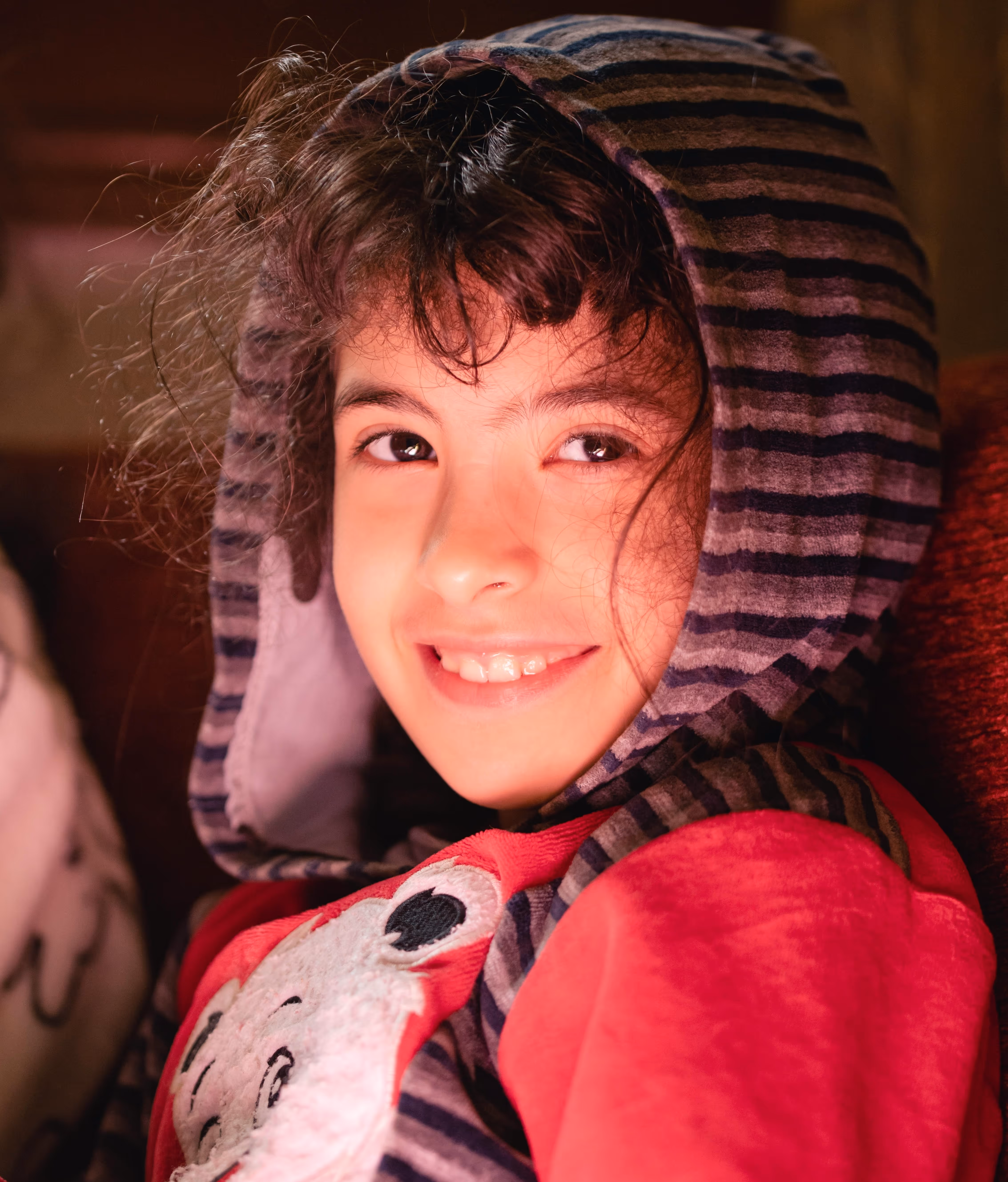 Child smiling indoors in a hooded top for an orphan relative visa application.
