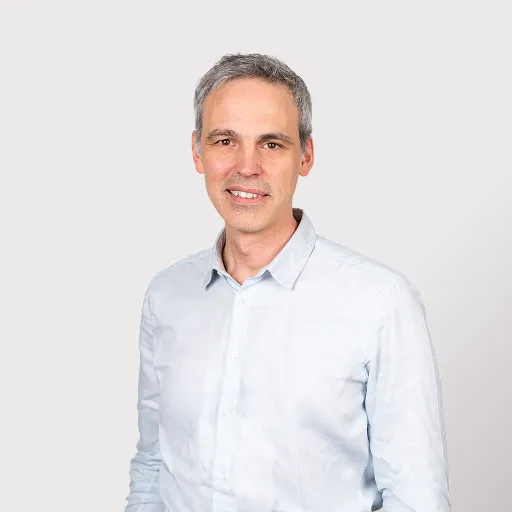 Middle-aged man with short gray hair wearing a light blue shirt smiling against a plain background.