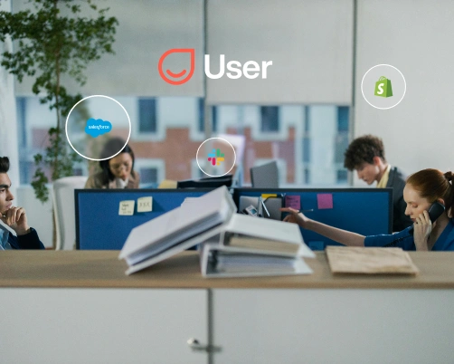 Office with four people working at desks and logos of User, Salesforce, Slack, and Shopify displayed.