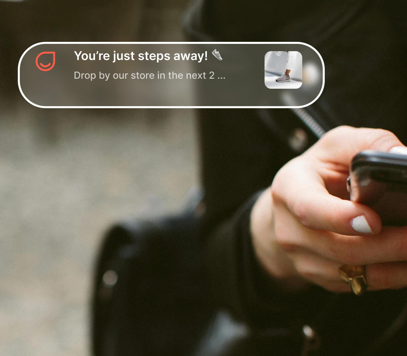 Hand with white nail polish holding a smartphone with a notification about visiting a store soon.