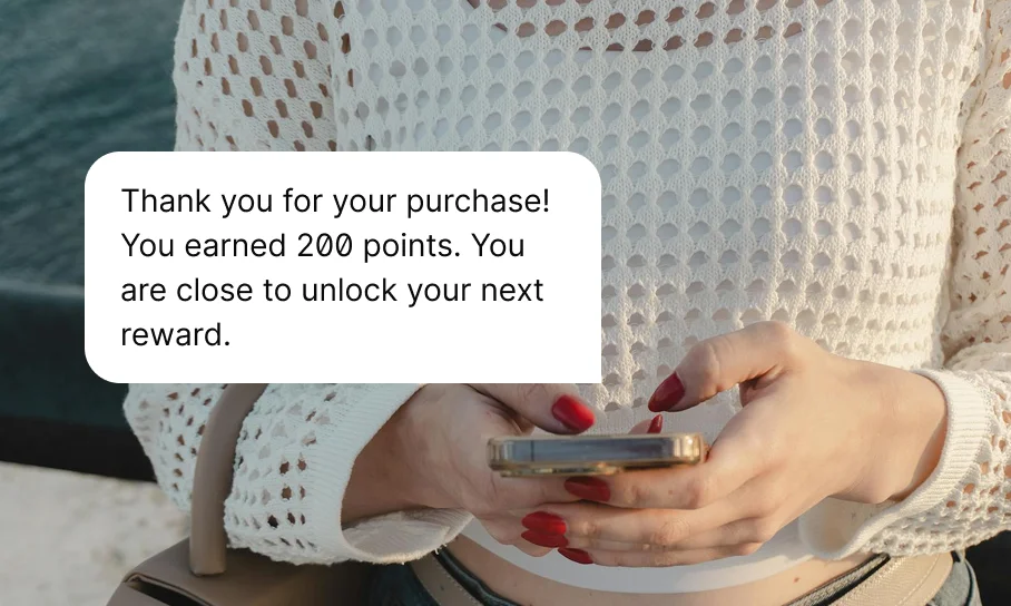 Person with red nail polish holding a phone and a loyalty message about points and rewards.