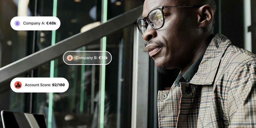 Man in glasses and checked coat looks at laptop with company data and account score overlays.