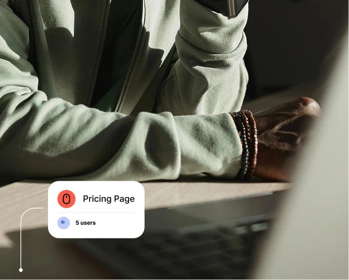 Person with a bracelet working at a table with laptop; overlay shows 'Pricing Page' with 5 users.