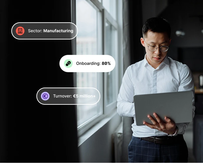 Man in glasses and white shirt holding a laptop near a window with business metric overlays.