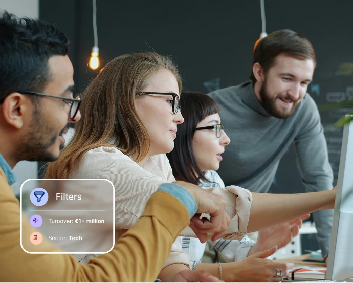 Four diverse coworkers wearing glasses collaborate enthusiastically around a computer screen in an office.