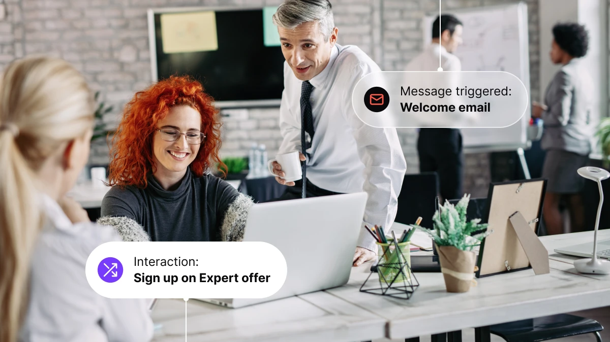 Three colleagues at a desk with a laptop; popups show "Sign up on Expert offer" and "Welcome email" messages.
