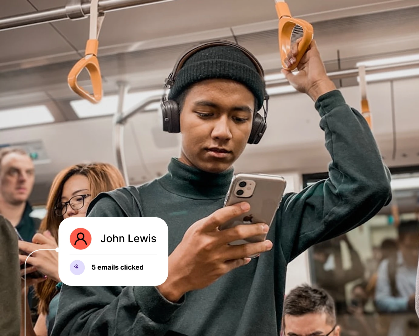 Young man wearing headphones and a beanie, holding a phone and standing on a crowded bus or train.