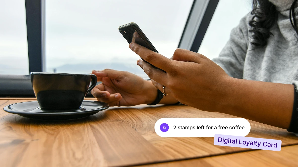 Person holding a phone near a coffee cup with a notification about 2 stamps left for free coffee.