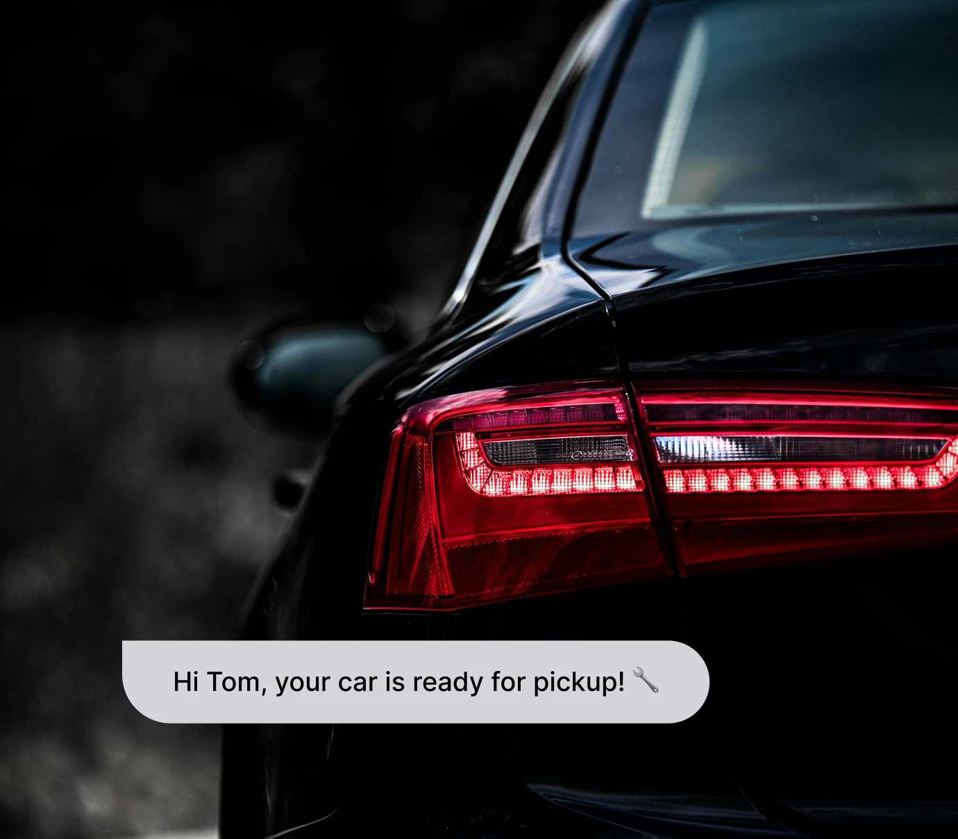 Close-up of a black car's illuminated rear tail light with a notification bubble about car pickup.