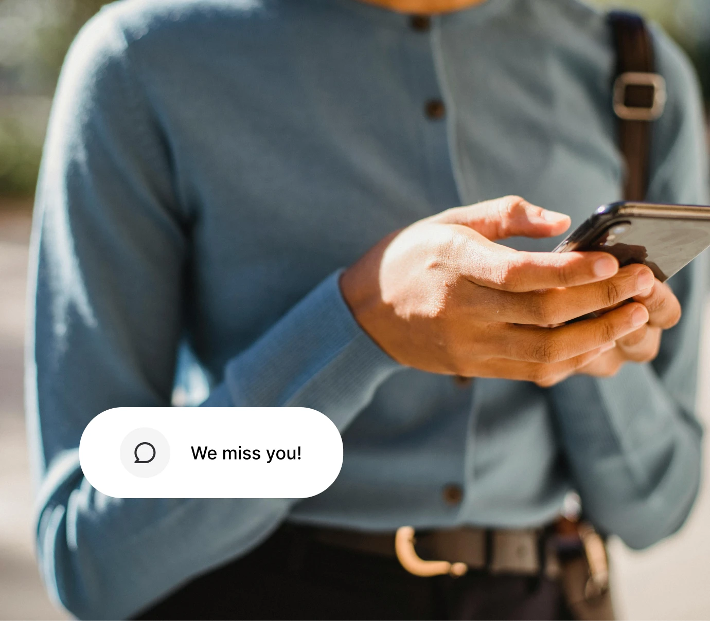 Person wearing blue sweater holding smartphone with message bubble saying We miss you!