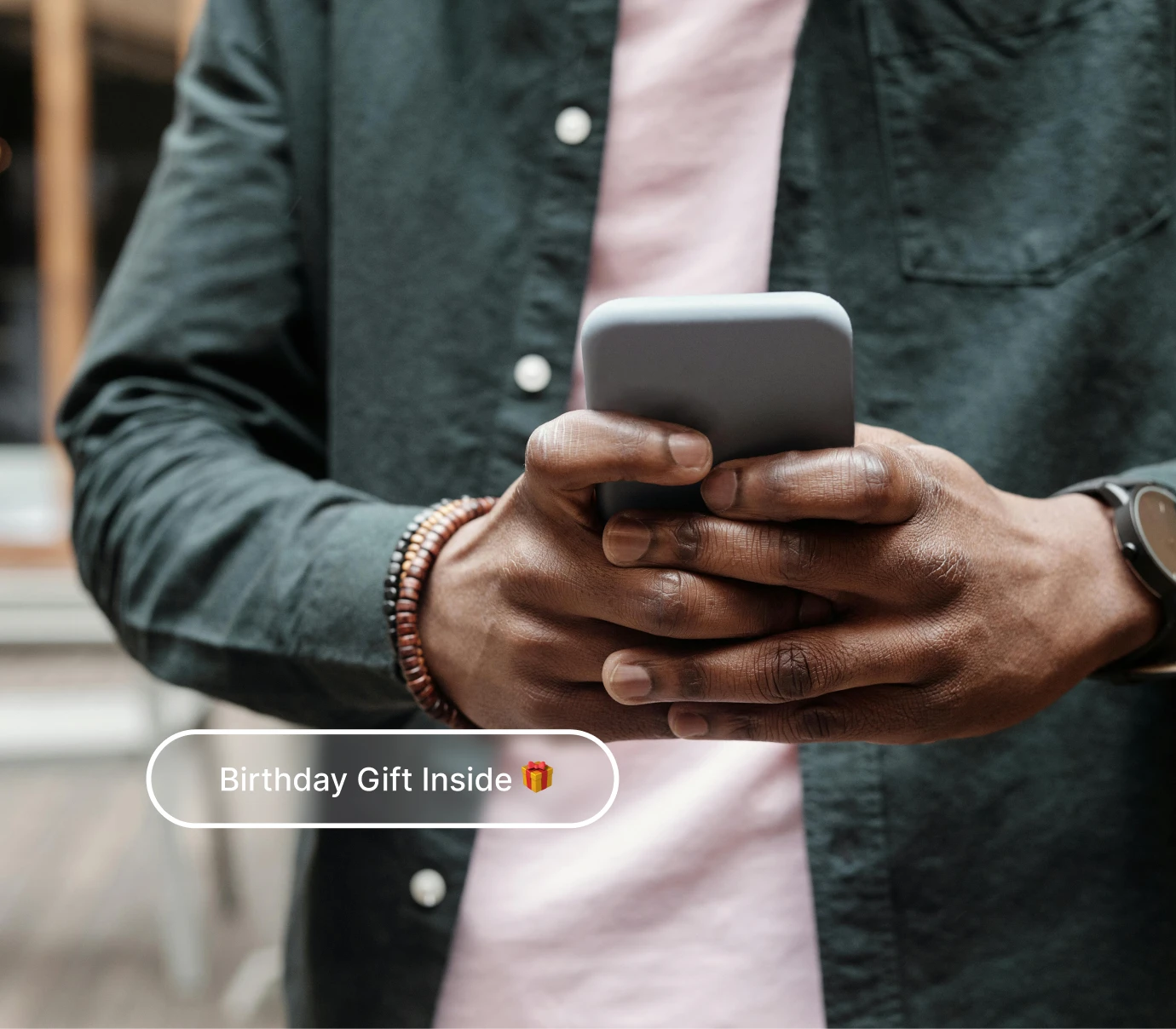 Person in dark green shirt holding a smartphone with text 'Birthday Gift Inside' and gift emoji.