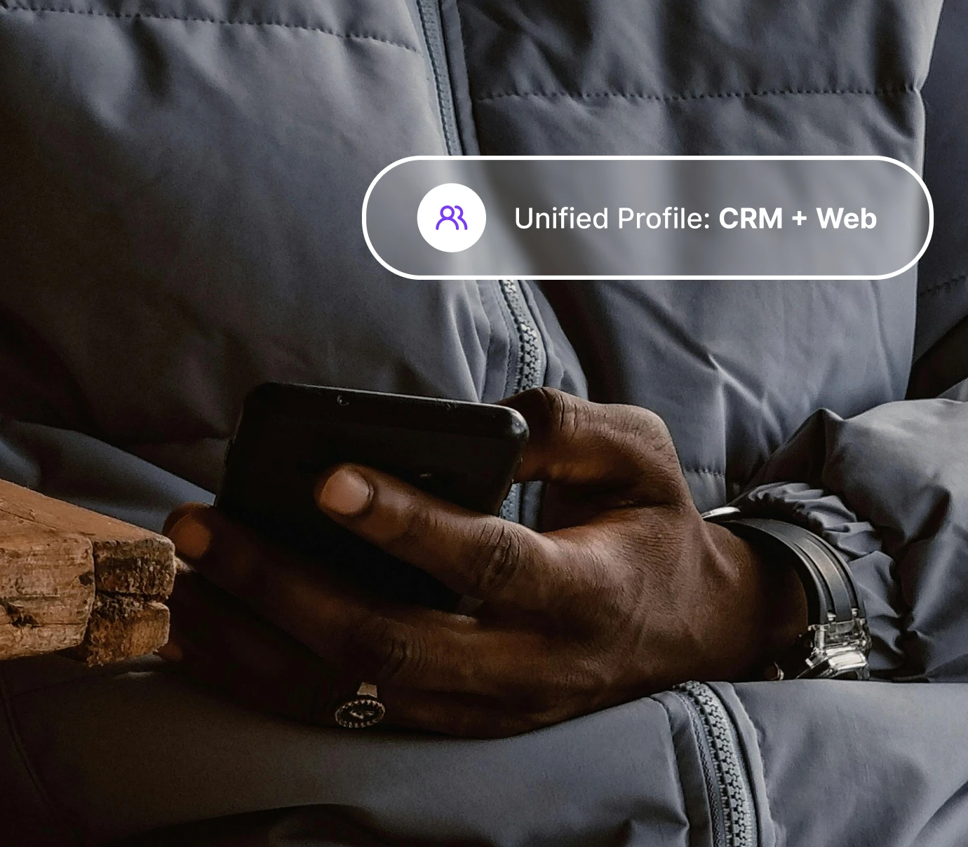 Person in gray jacket holding a smartphone with text overlay about unified profile CRM plus web.