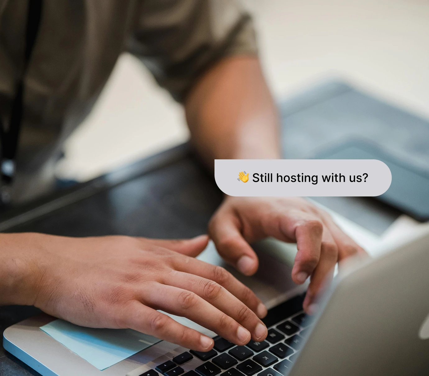 Hands typing on a laptop keyboard with a chat bubble saying, 'Still hosting with us?'