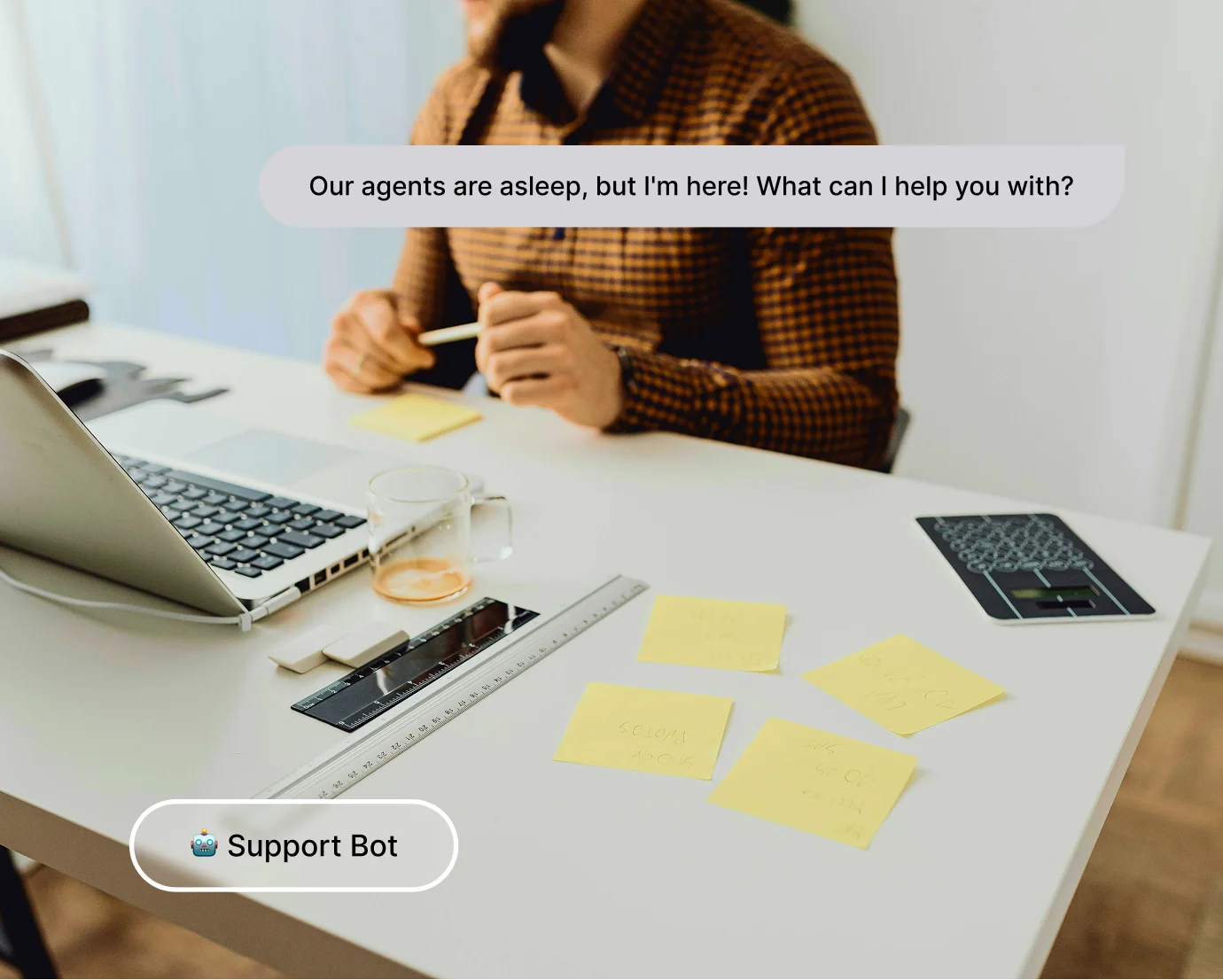 Man in checkered shirt at desk with laptop, sticky notes, and chatbot message offering help.
