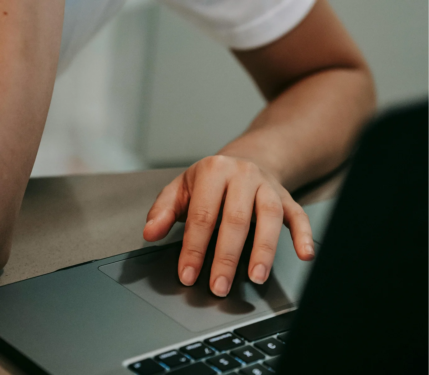Person's hand resting on a laptop trackpad with part of the keyboard visible.