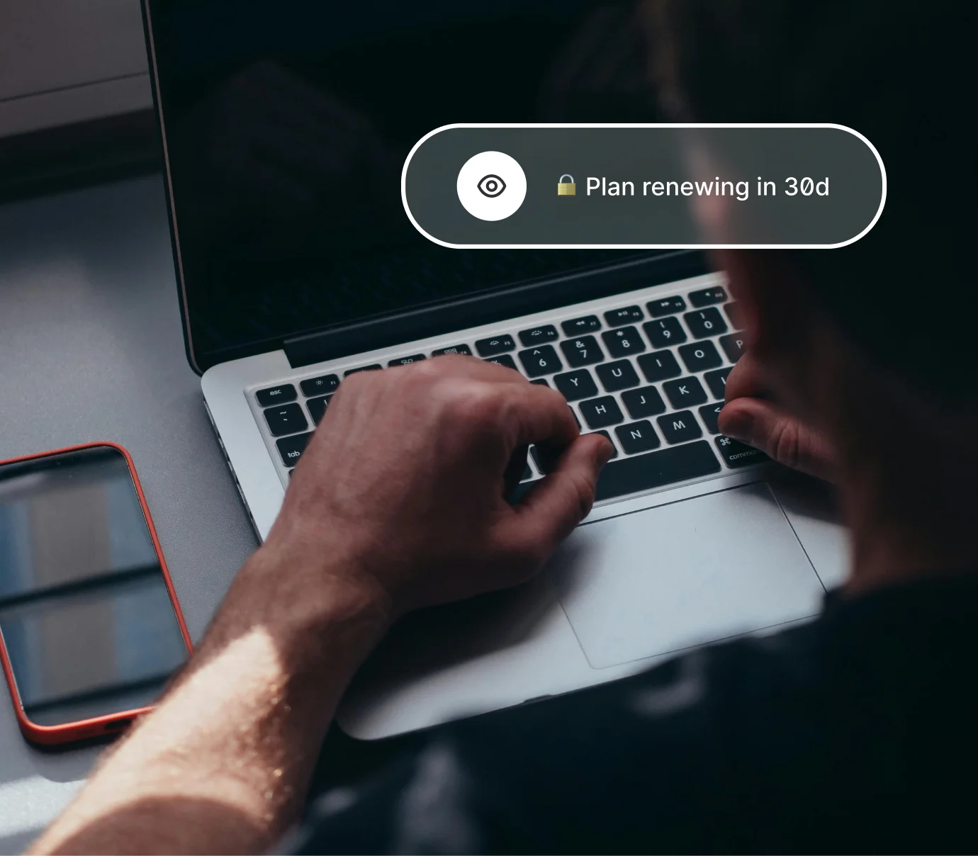 Person typing on laptop keyboard with smartphone on desk and screen text about plan renewing in 30 days.