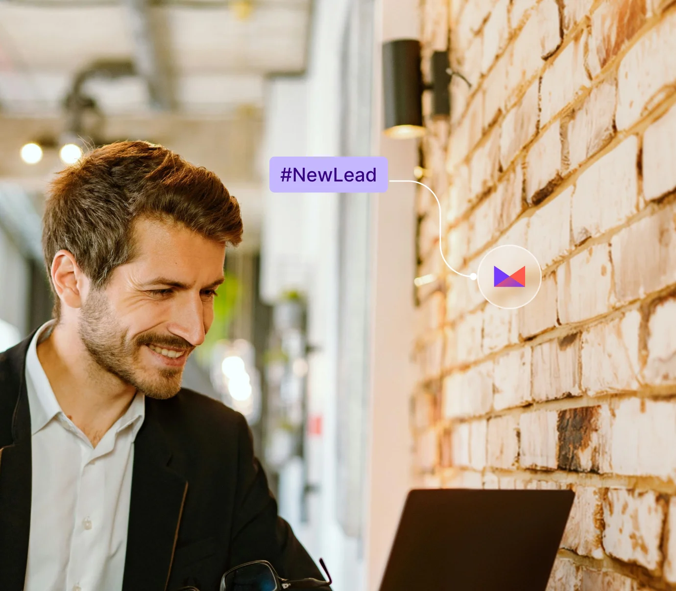 Smiling man in blazer looks at laptop indoors against a white brick wall with #NewLead graphic.
