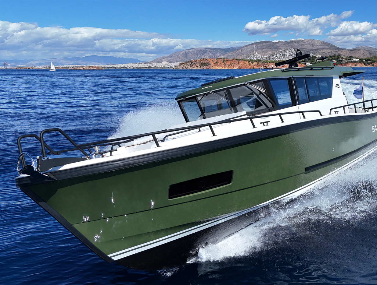 Green and white motorboat speeding on blue water with mountains and cloudy sky in the background.
