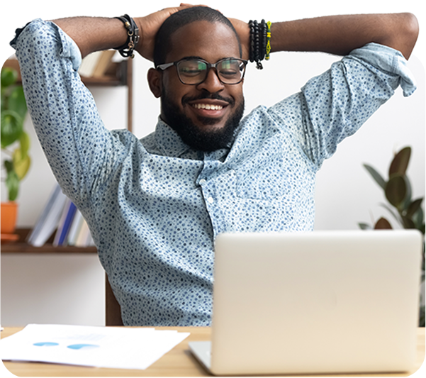 Man sat at desk smiling with arms behind his head looking relaxed at his laptop