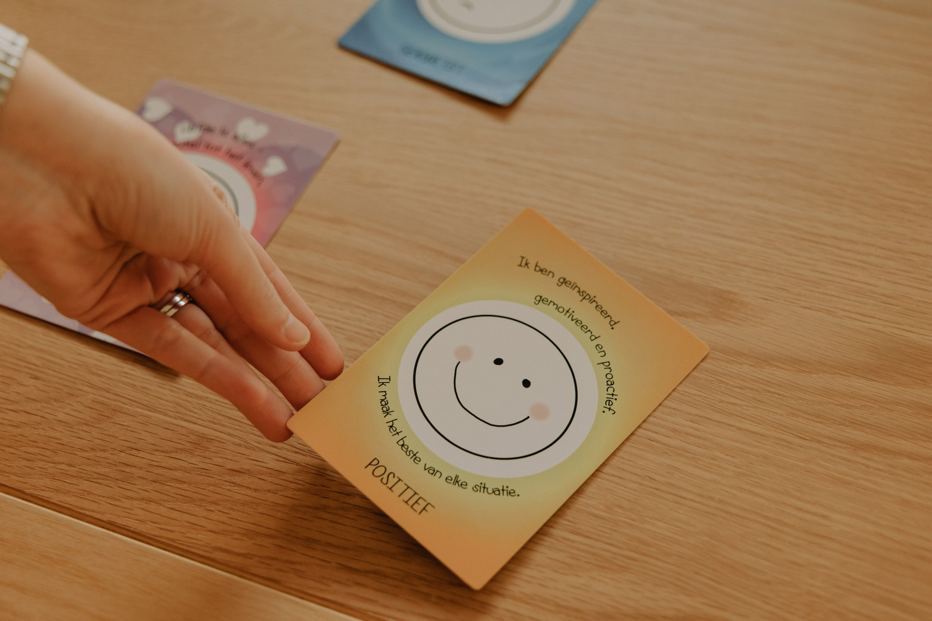 Hand die een kaart vasthoudt met een glimlachend gezicht en de woorden 'Ik ben geïnspireerd, gemotiveerd en proactief. Ik maak het beste van elke situatie. POSITIEF'.