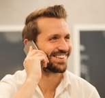 Smiling man with beard talking on a smartphone indoors.