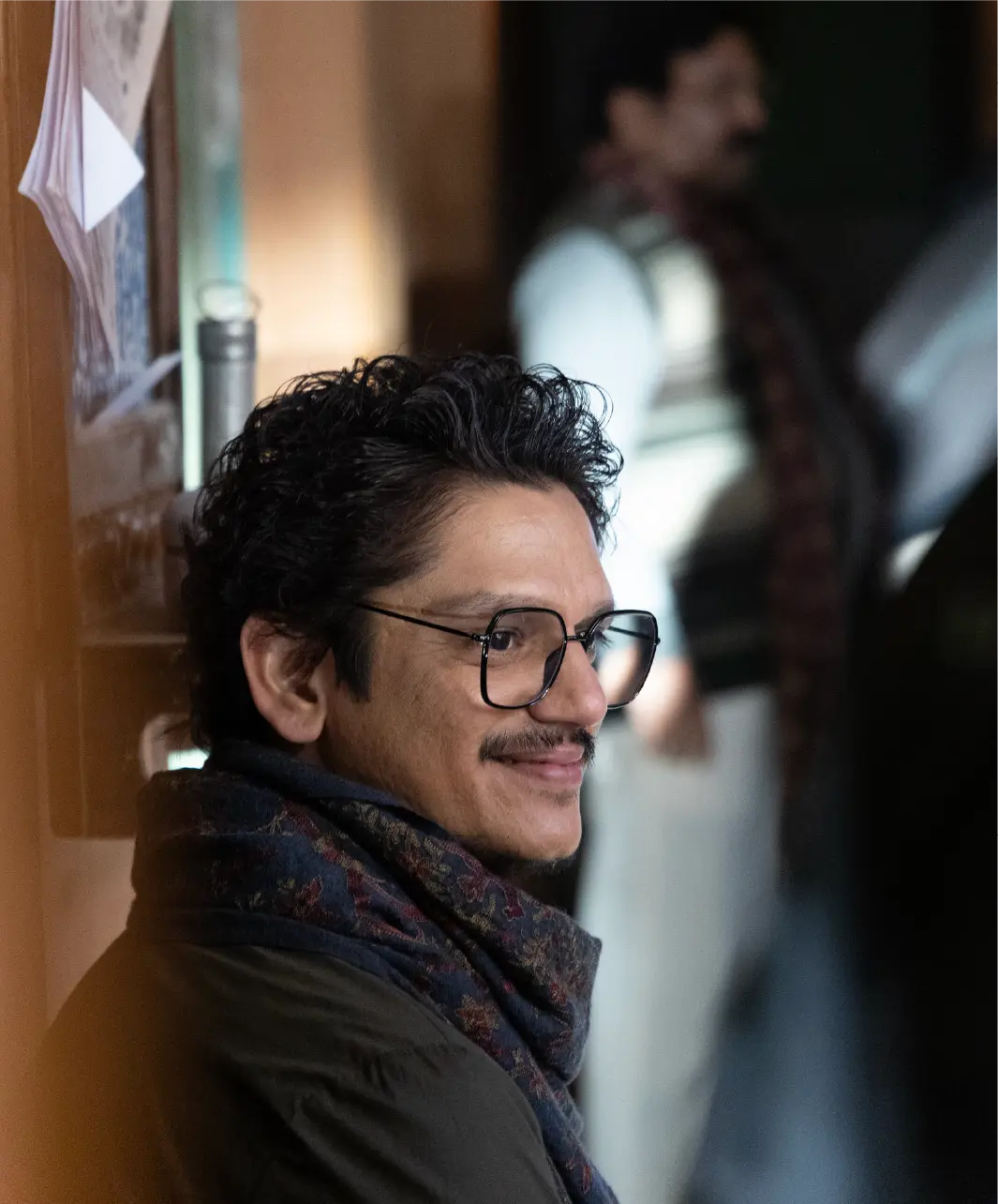 A production still from Gustaakh Ishq featuring Vijay Varma as Pappan; he is wearing glasses and a patterned scarf, smiling warmly in an indoor setting.