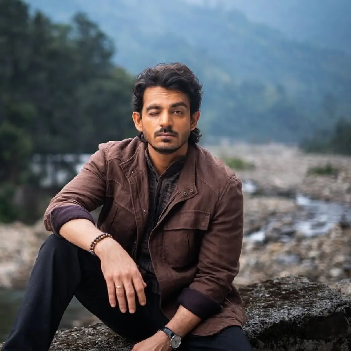 Actor Anshumaan Pushkar sitting on a rocky ledge in a production still for the film Saali Mohabbat, directed by Tisca Chopra.