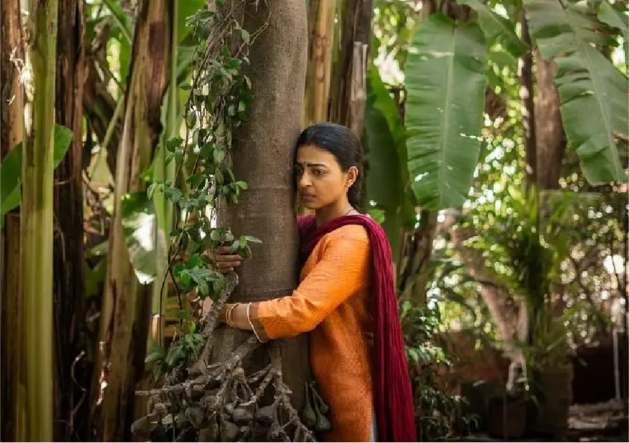 adhika Apte with a distressed expression holding onto a thick tree in a tropical garden setting; a cinematic shot from the movie Saali Mohabbat.