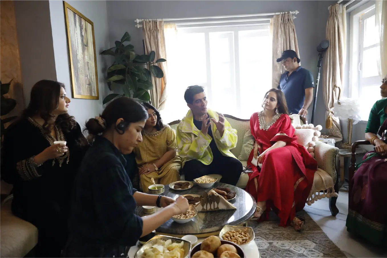 Behind-the-scenes still of Manish Malhotra on the indoor set of Saali Mohabbat; cast and crew gathered around a table with snacks.