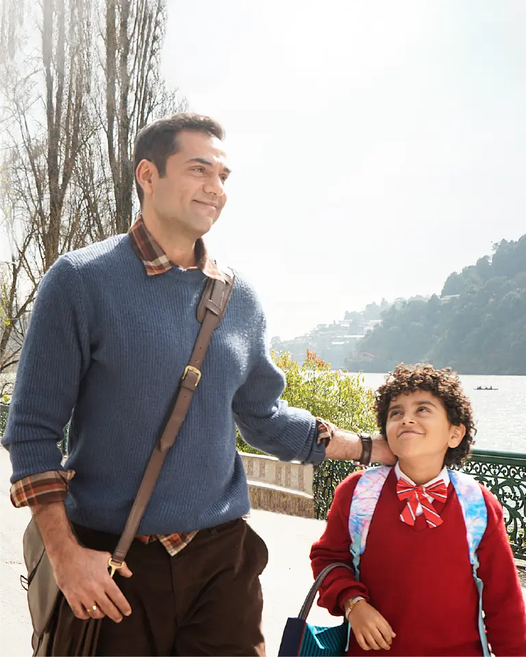 Abhay Deol and Rohaan Singh walking along a scenic lakeside path with mountains in the background in a production still for Bun Tikki.