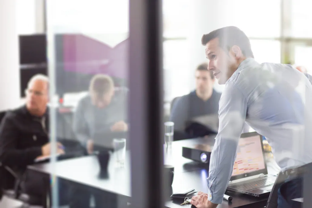 A man presenting in a business meeting, viewed through a glass wall.