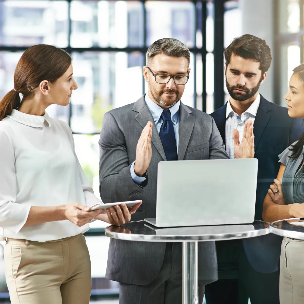 Four professionals discussing around a laptop in an office setting.