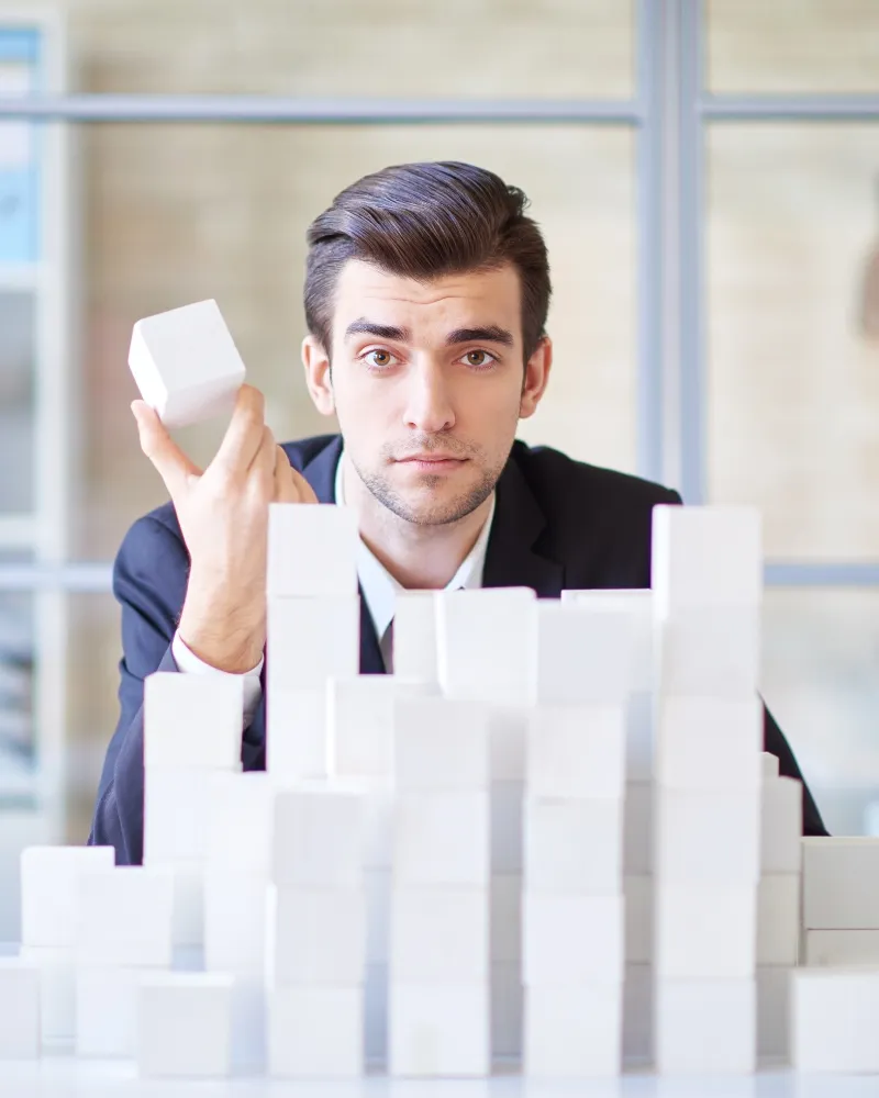 Man examining a white block in front of a structure made of similar blocks.