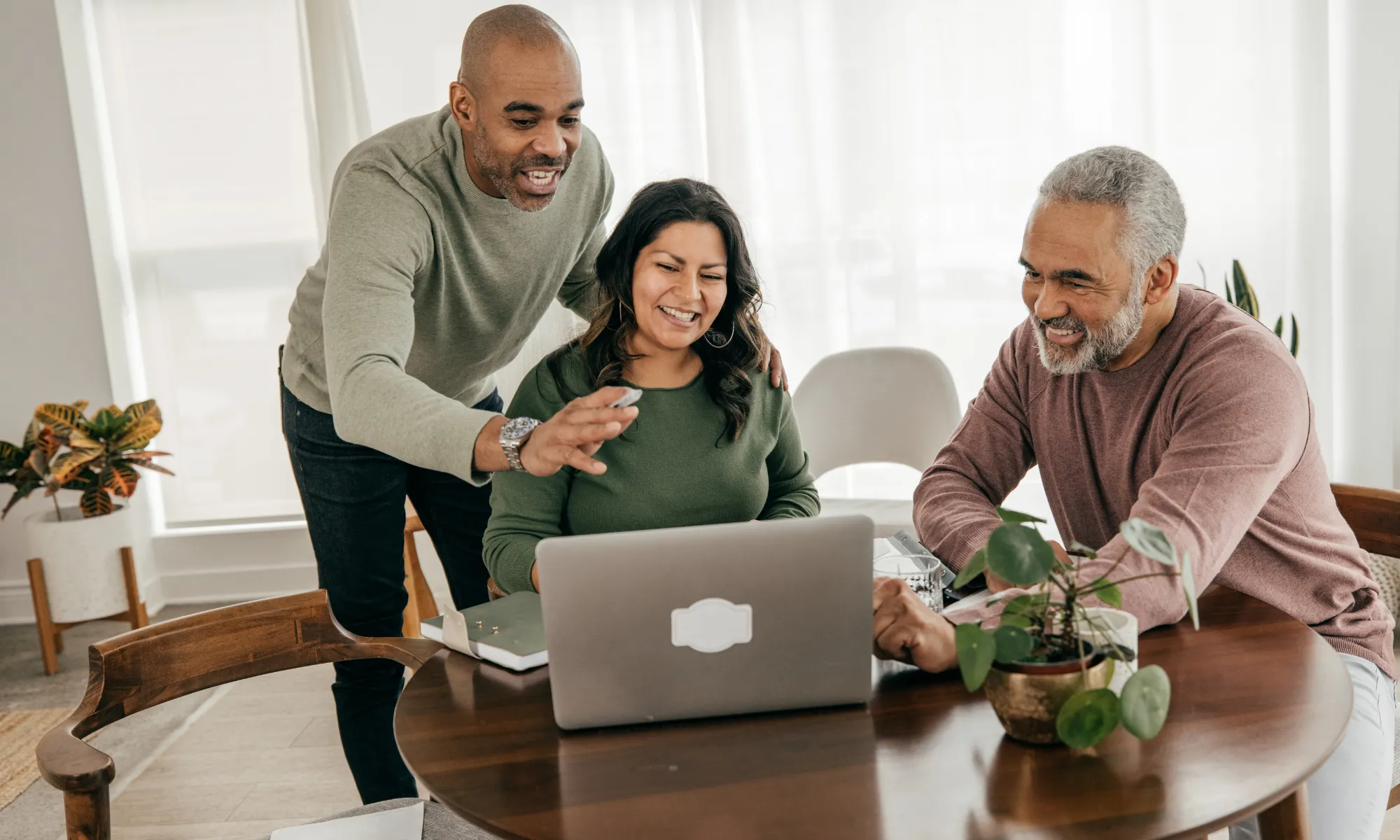 Three adults sharing a light-hearted moment around a laptop in a bright home office.