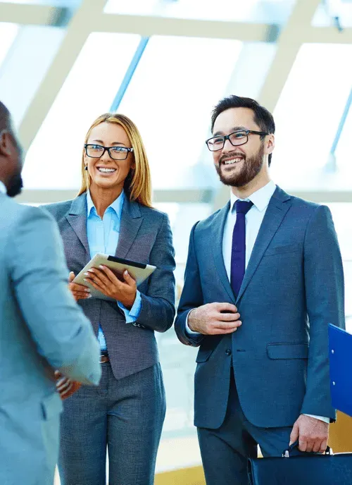Two professionals in business attire smiling during a conversation with a colleague.