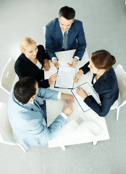 Four business professionals engaged in a meeting around a table with documents and a phone.