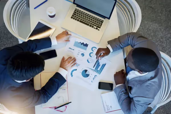 Two business valuation specialists discussing graphs and charts in a business meeting from a top-down perspective.