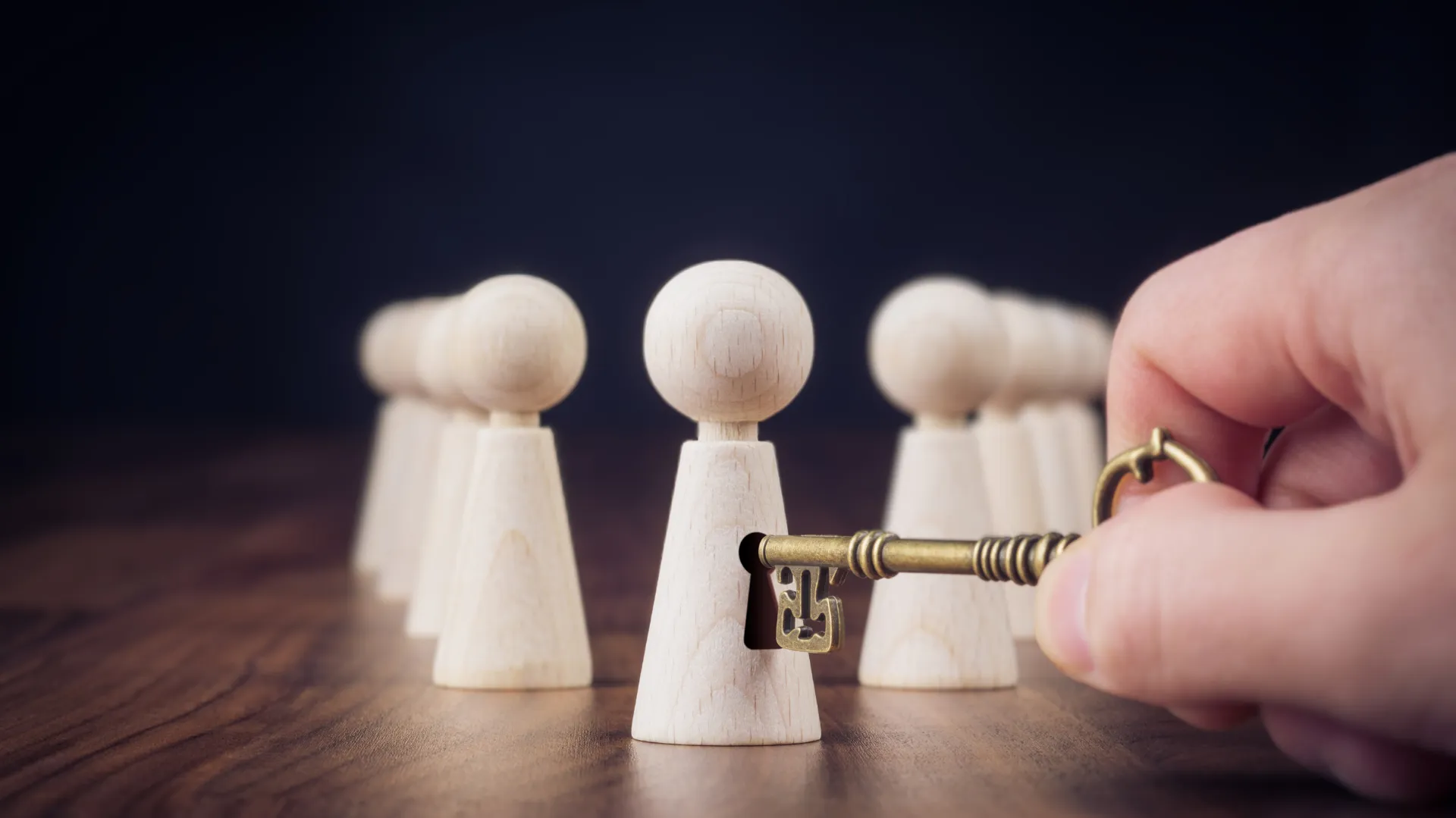 A hand holding a key towards wooden figures, symbolizing unlocking potential or providing access.