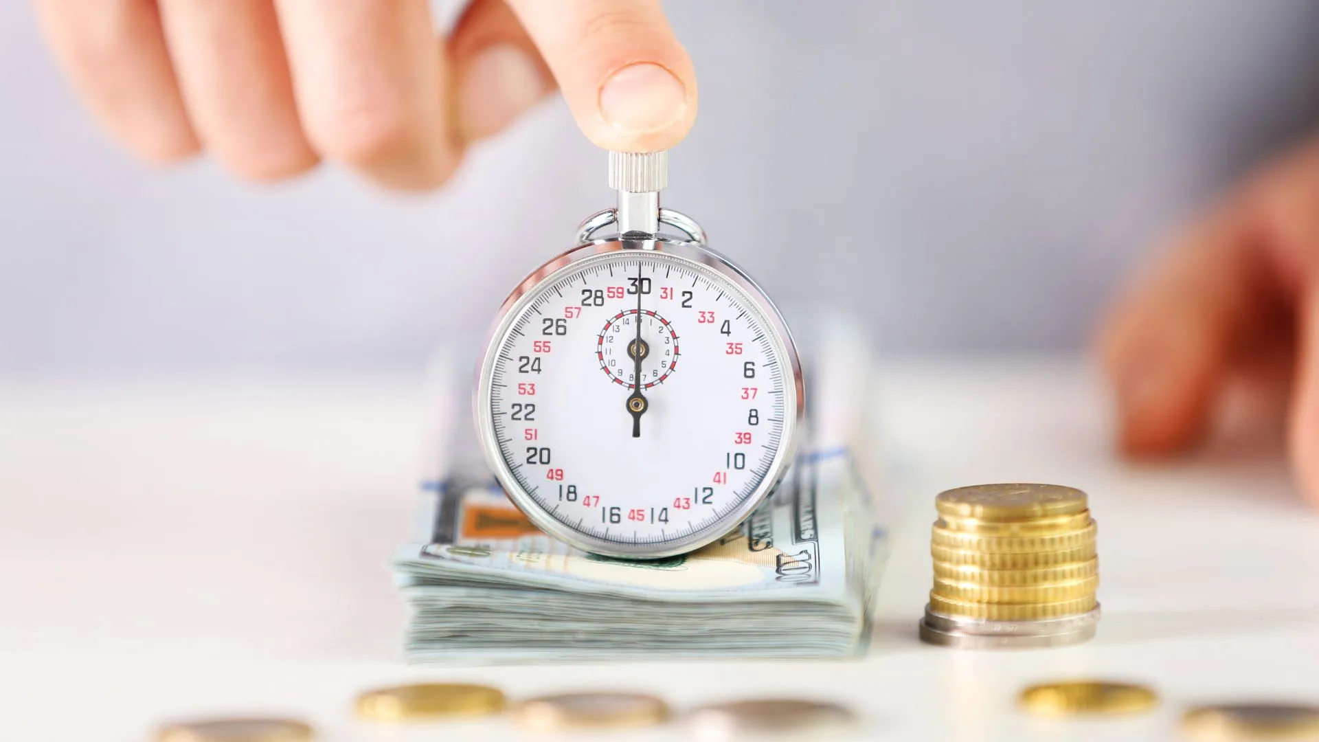 Person placing a coin on a stack of money with a stopwatch, illustrating the concept of time-sensitive investment or savings growth.