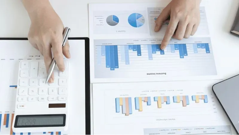 A group of people working on spreadsheets and graphs on a desk.