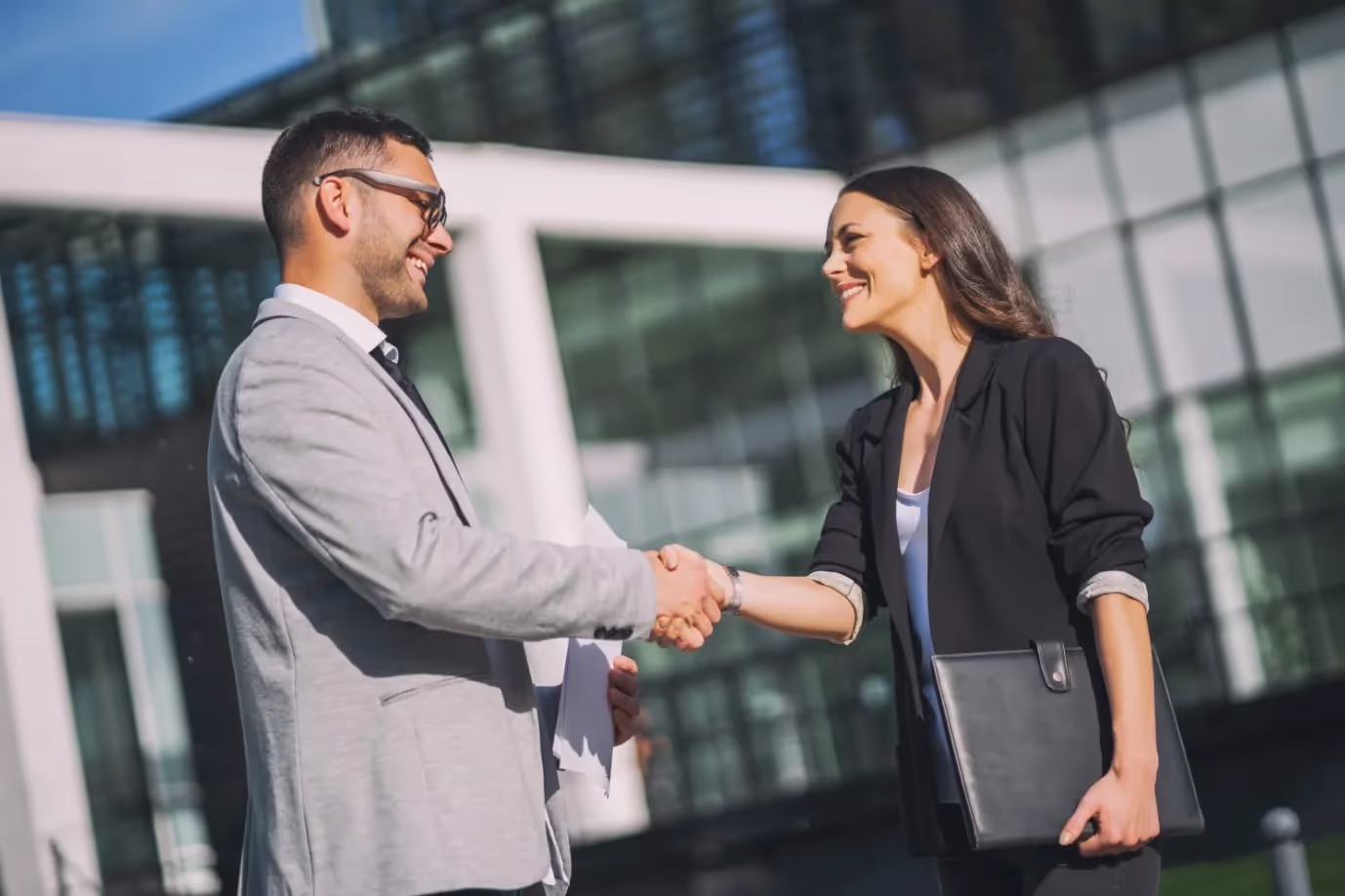 Two business brokers shaking hands in front of a building.