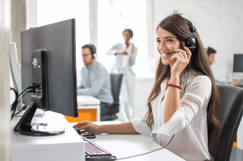 A VNB Business Brokers customer service representative wearing a headset and sitting at a desk with a computer speaking to a client.