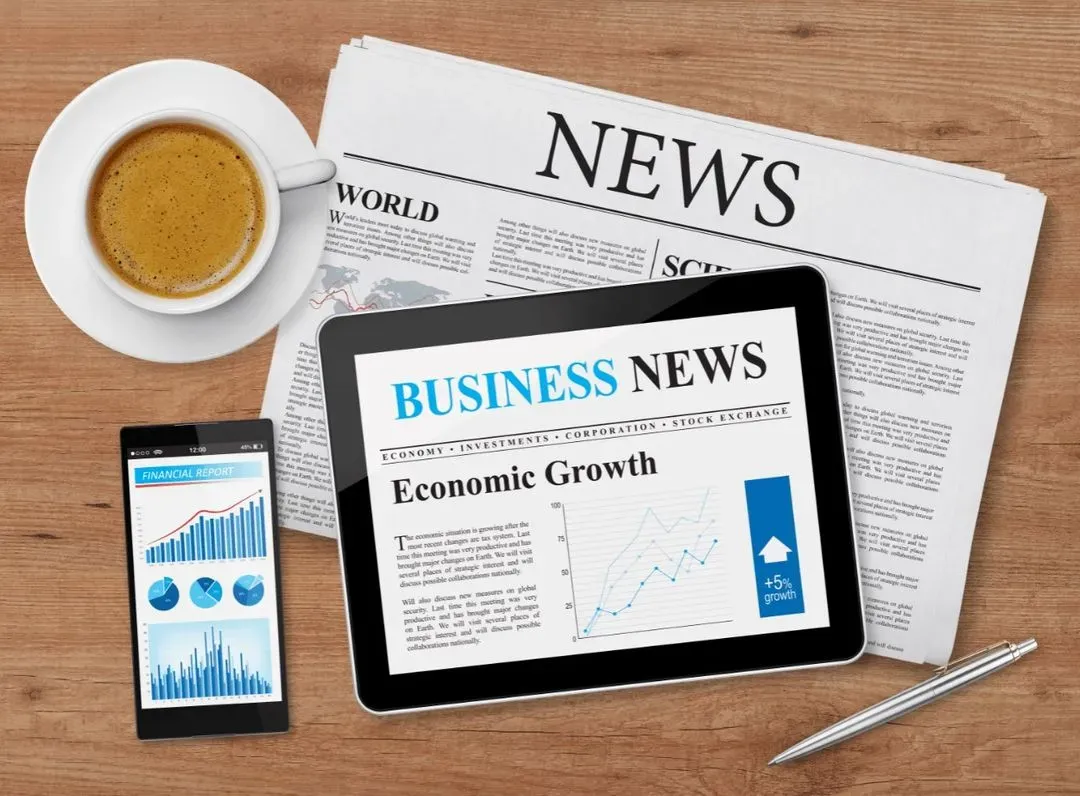 A tablet with business news and a cup of coffee on a wooden table.