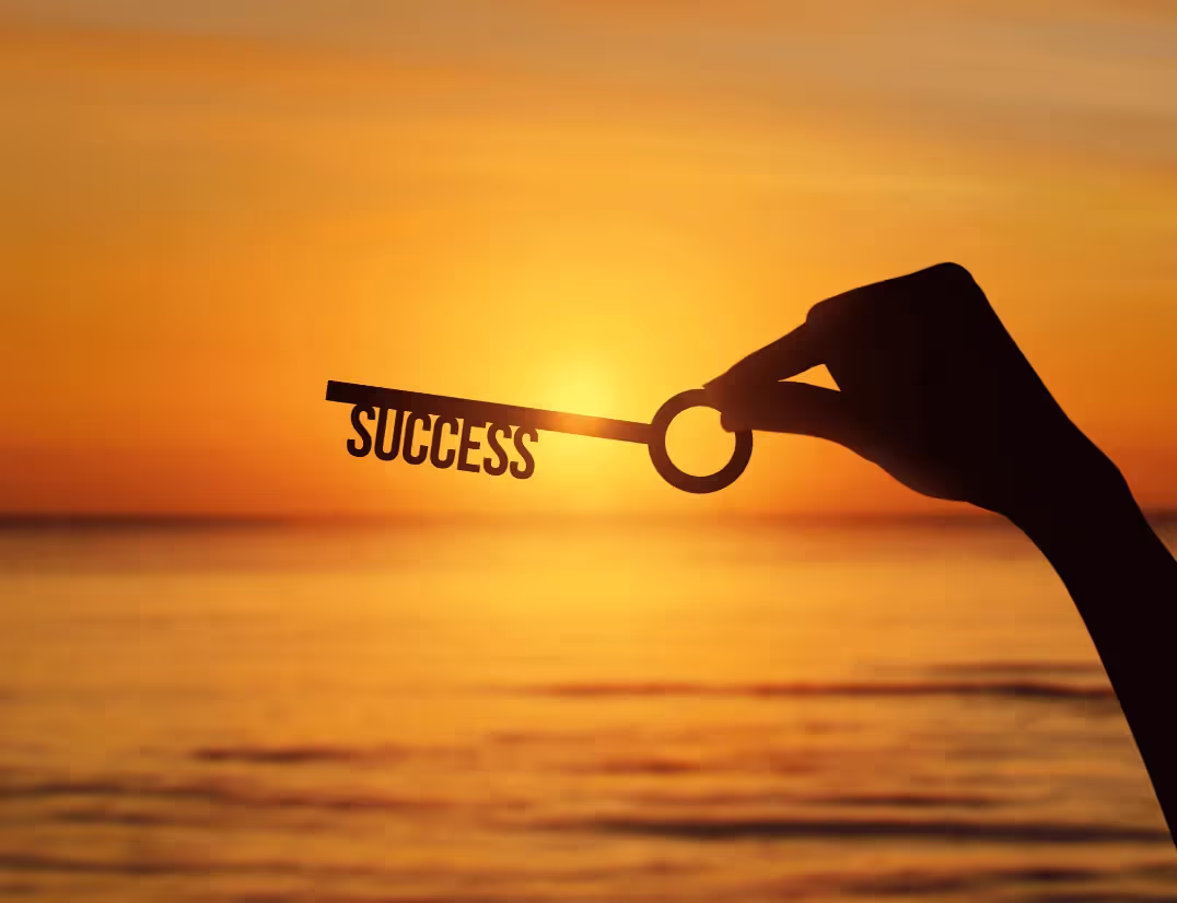 A person holding a key with the word "success" in front of a sunset.
